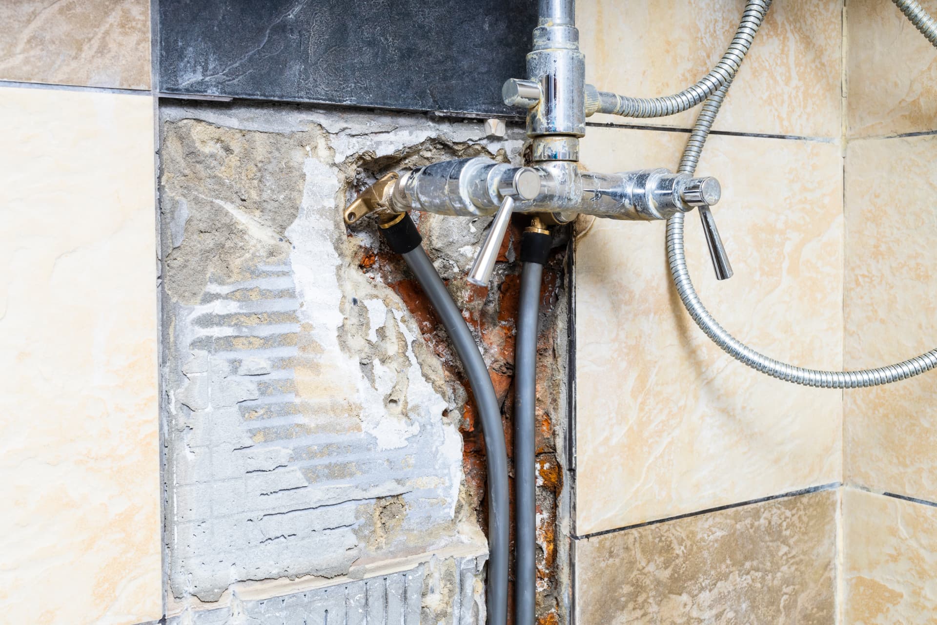 Shower valve and supply lines exposed behind damaged bathroom tile