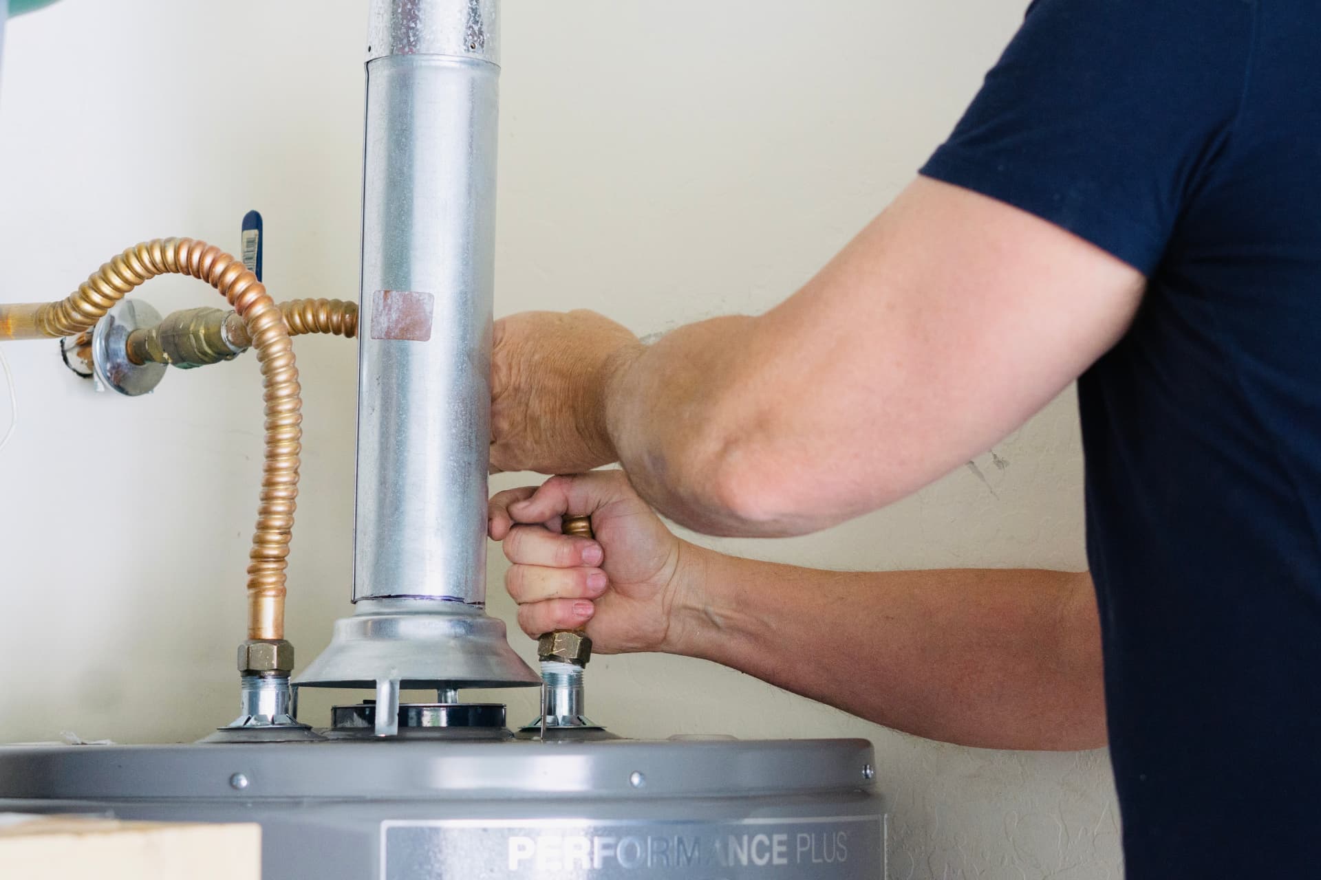 Plumber tightening the gas supply fitting on a residential water heater